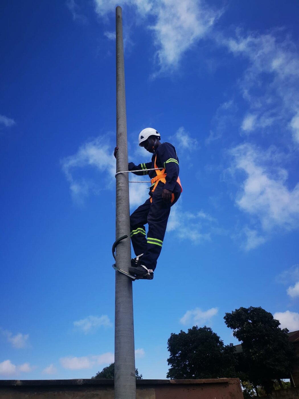 Technician safely climbing an OMBRA FRP pole using climbing spikes and a harness
